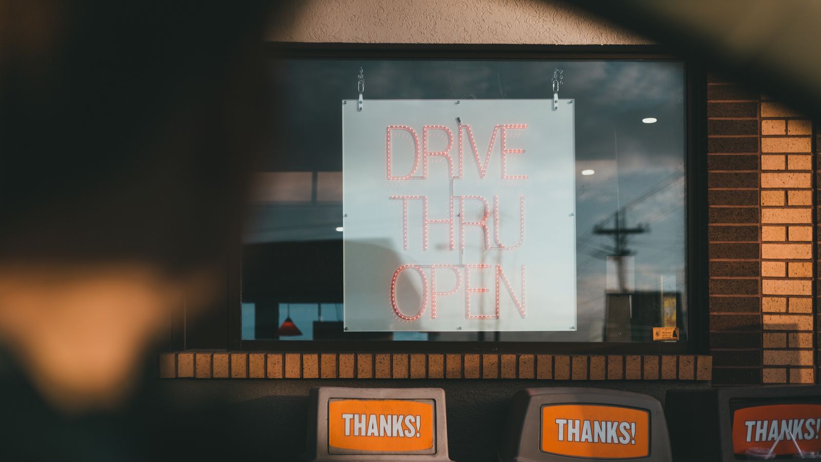 Blurred crop faceless male sitting in automobile near window of public cafe with Drive Thru Open inscription while making contactless order