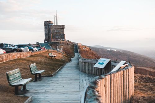Free Boardwalk with wooden benches near parked card leading to historic stone fortress on Signal hill of Canada against cloudless sky Stock Photo