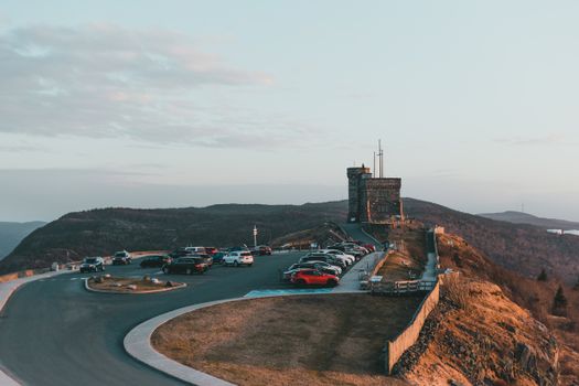 Automobiles parked on asphalt road near famous historic stone fortification located on grassy Signal hill in nature against cloudy sky
