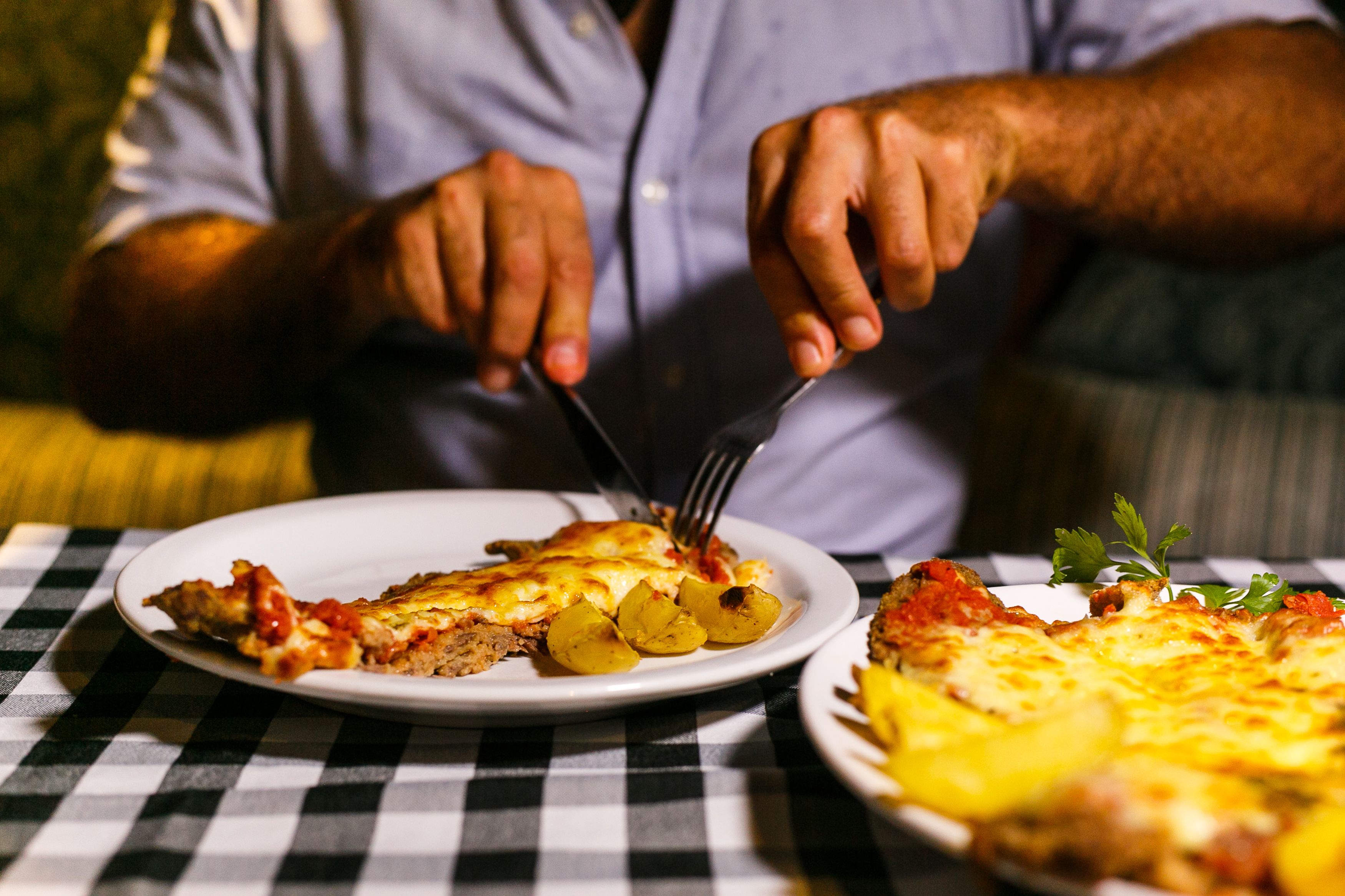 A person cutting and serving a cheesy pizza with crispy potatoes, shot indoors.