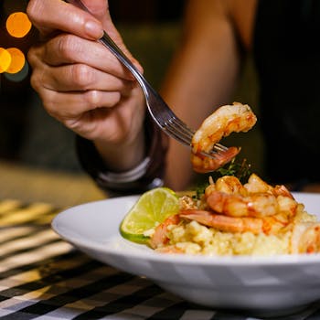 Close-up of a hand holding a fork with shrimp from a flavorful seafood dish.