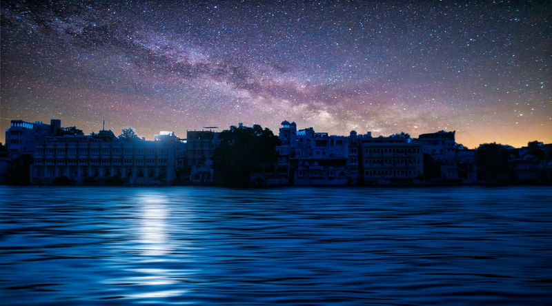 A stunning view of the Milky Way over Udaipur city reflected in the lake at night.