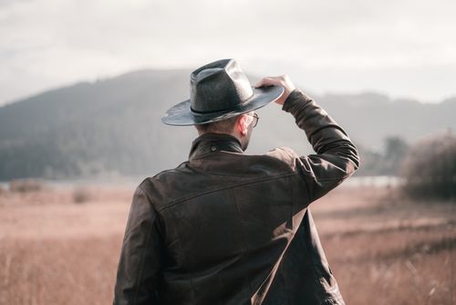 Free Back view of a man in a leather jacket and hat looking over a scenic landscape. Stock Photo