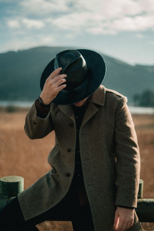 Free A man in a fashionable coat and hat poses stylishly outdoors against a scenic backdrop. Stock Photo