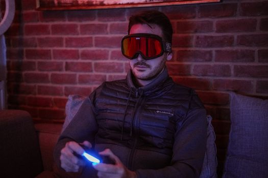 A man wearing futuristic goggles plays video games indoors, focused and intense.