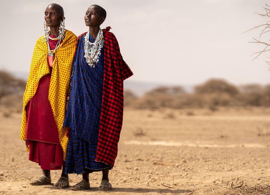 Masai individuals wearing vibrant traditional robes stand in the Tanzanian desert.