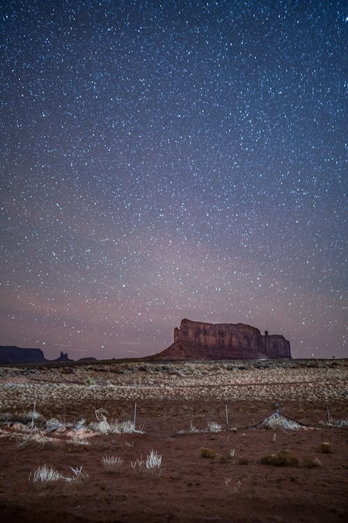 Picturesque scenery of grassy terrain near rough rocky formations in Monument Valley under starry sky in twilight