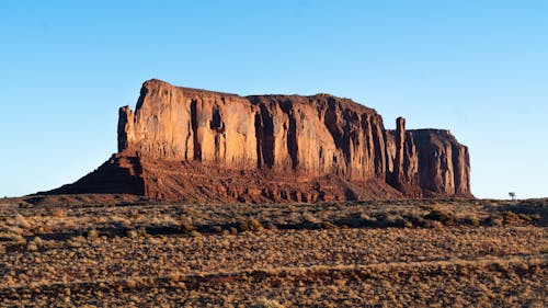 Picturesque scenery of grassy field near rough rocky formations in Monument Valley located in United States in sunny day