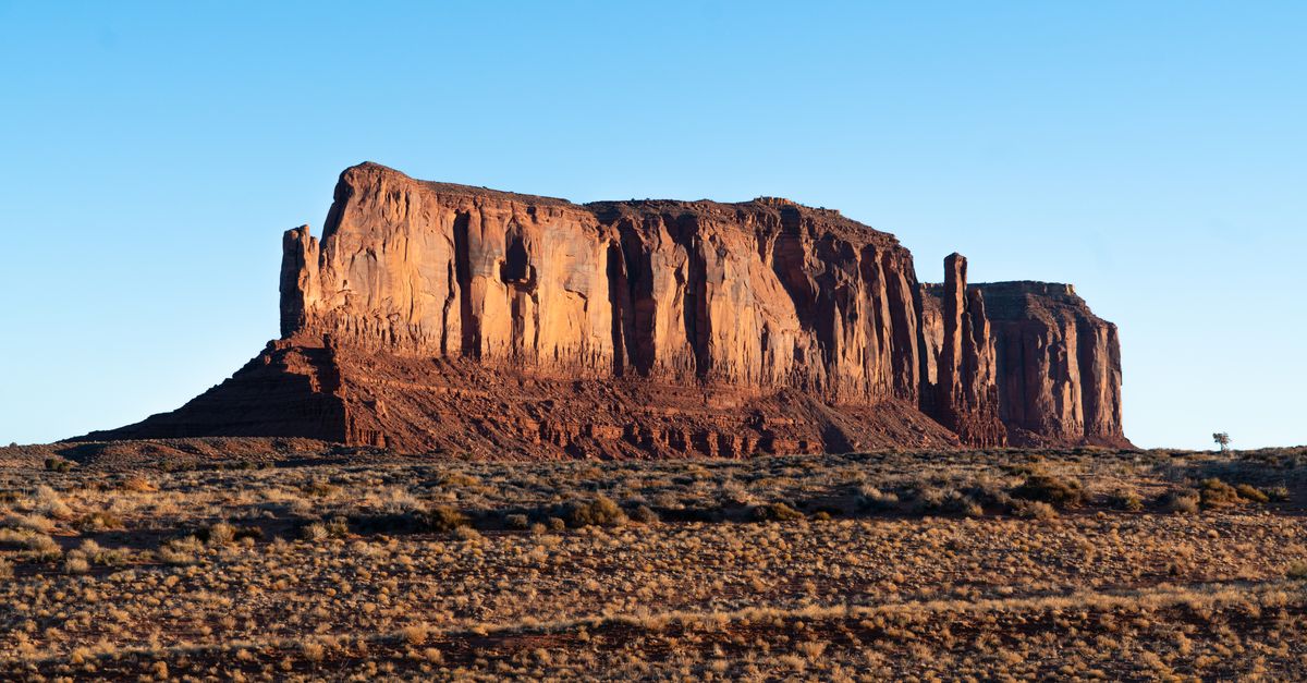 Picturesque scenery of grassy field near rough rocky formations in Monument Valley located in United States in sunny day
