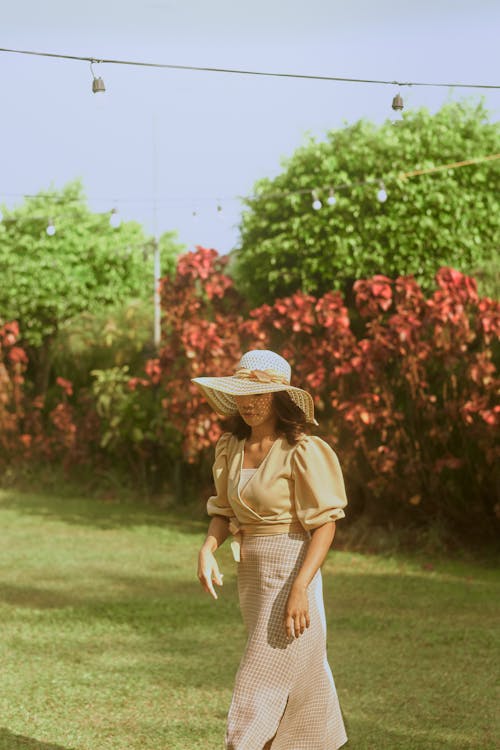 Woman Wearing Sun Hat Walking on Green Grass 