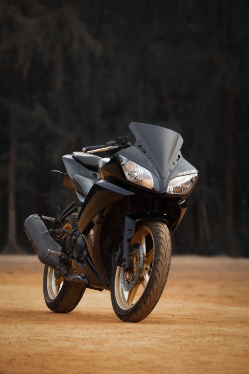 Free A sleek sports bike parked on a sandy surface against a dark forest background. Stock Photo