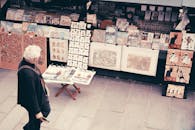 一位老人在巴黎街头市场欣赏艺术版画，感受城市文化氛围