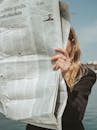 A Woman Reading a Newspaper Near Body of Water