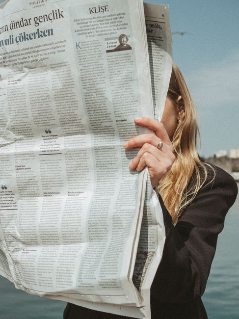 A woman in a black blazer reads a large newspaper by the water in Istanbul, Turkey.