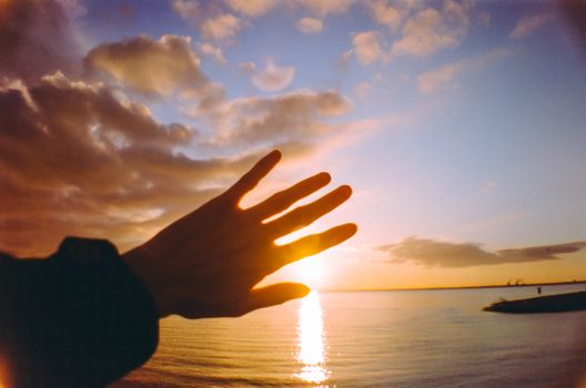 Silhouette of a hand against a vibrant sunset over the ocean, creating a serene and peaceful scene.