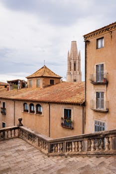 A scenic view of Girona's historic buildings and iconic church tower under a cloudy sky.