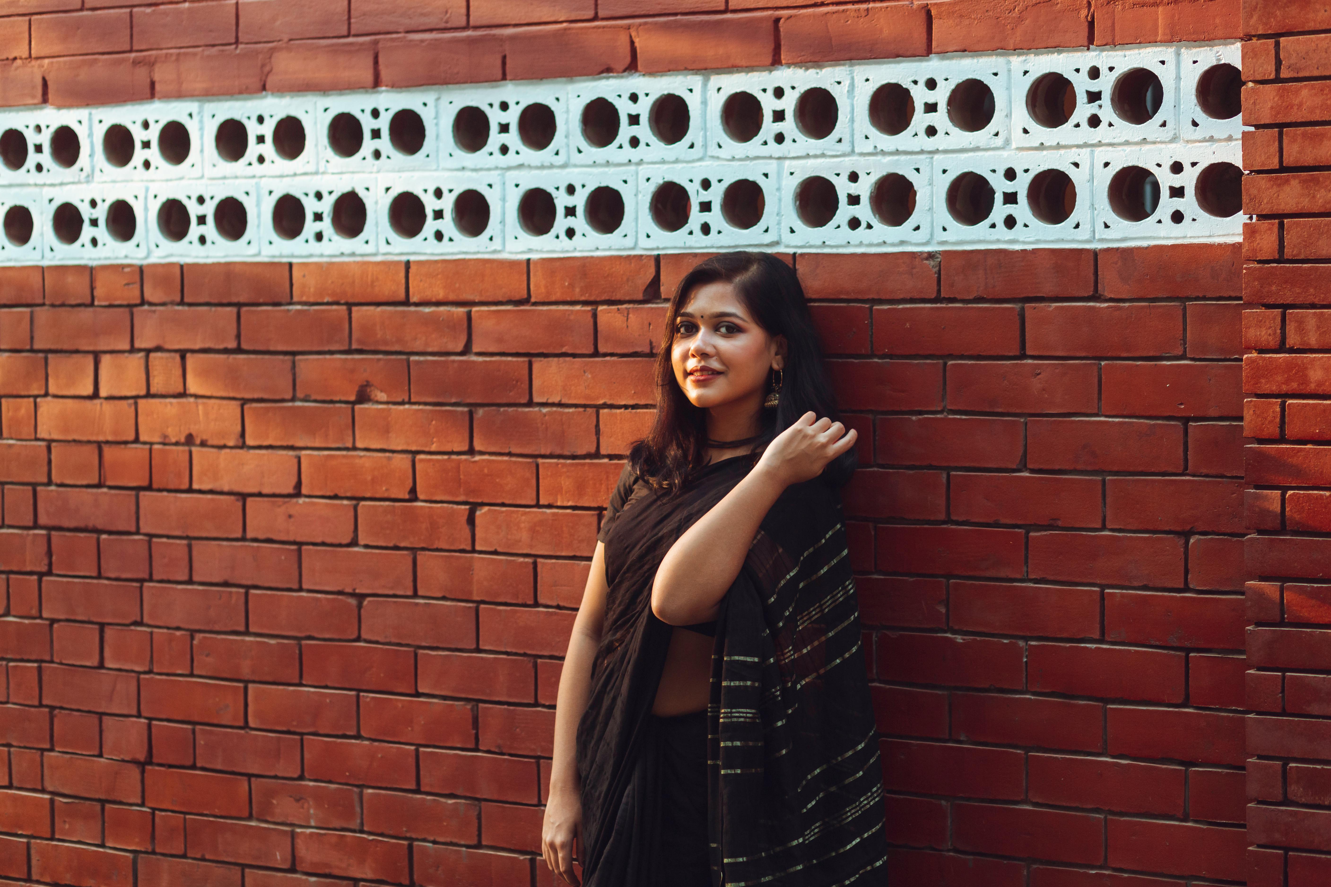 Woman in traditional black sari posing by a brick wall in Dhaka, Bangladesh.