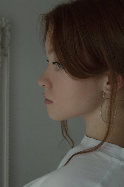 Side view of crop tranquil female with blue eyes wearing white shirt thoughtfully looking away