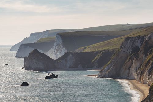 Free Stunning coastal landscape featuring rugged cliffs and serene sea under bright daylight. Stock Photo