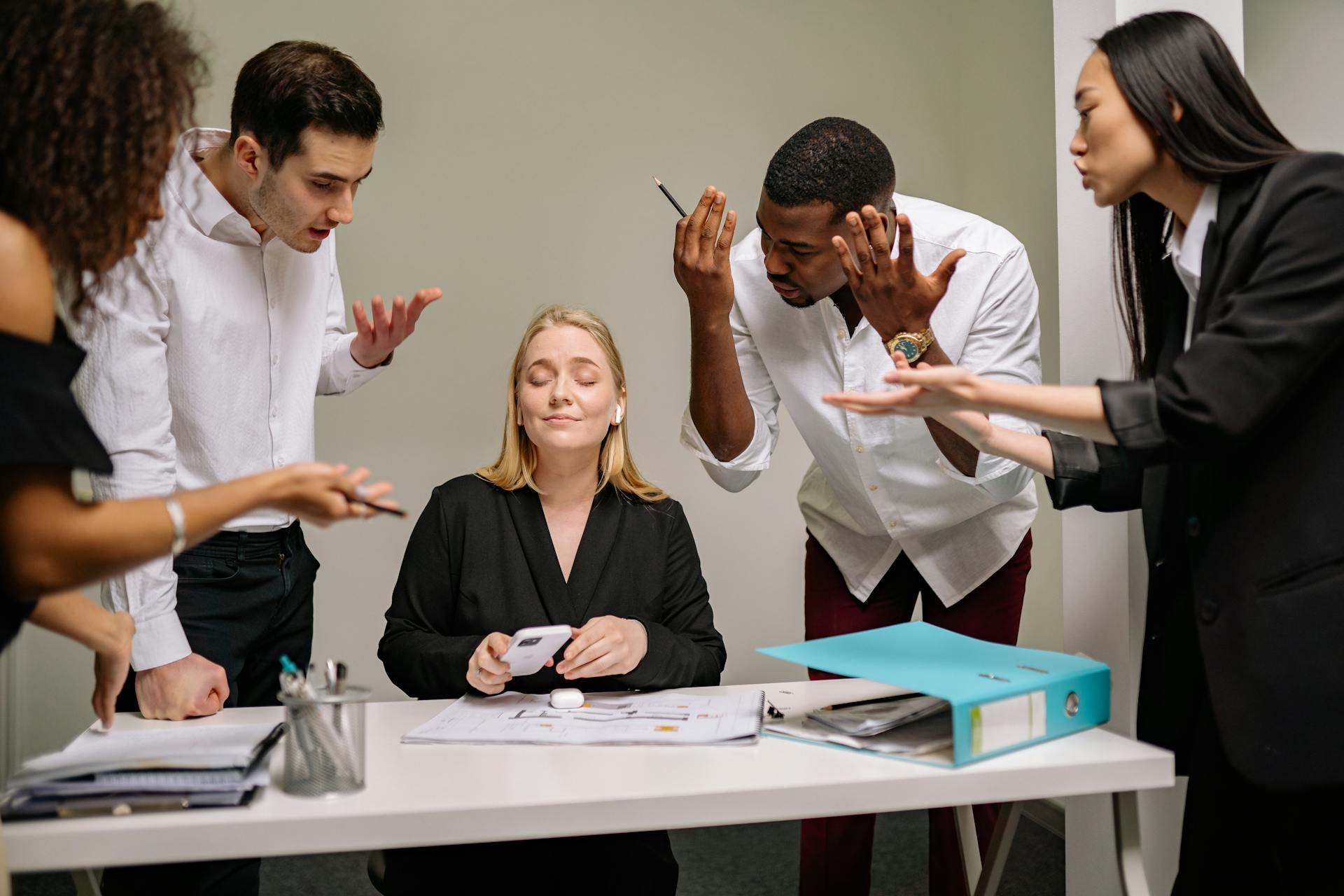 A diverse team of professionals engaged in a dynamic office discussion around a desk.