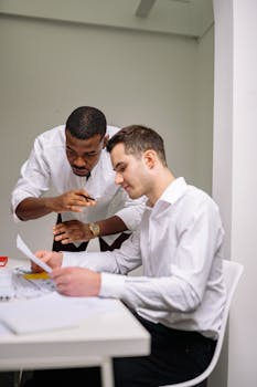 Two business professionals in a modern office engaged in a paper discussion.