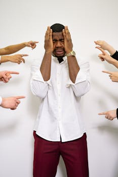Anxious businessman in corporate attire surrounded by pointing fingers, shows workplace pressure.