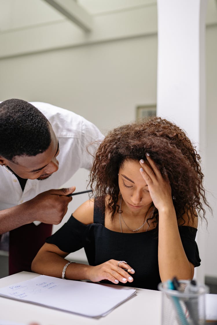 A Man Scolding A Woman Sitting At A Table With Documents