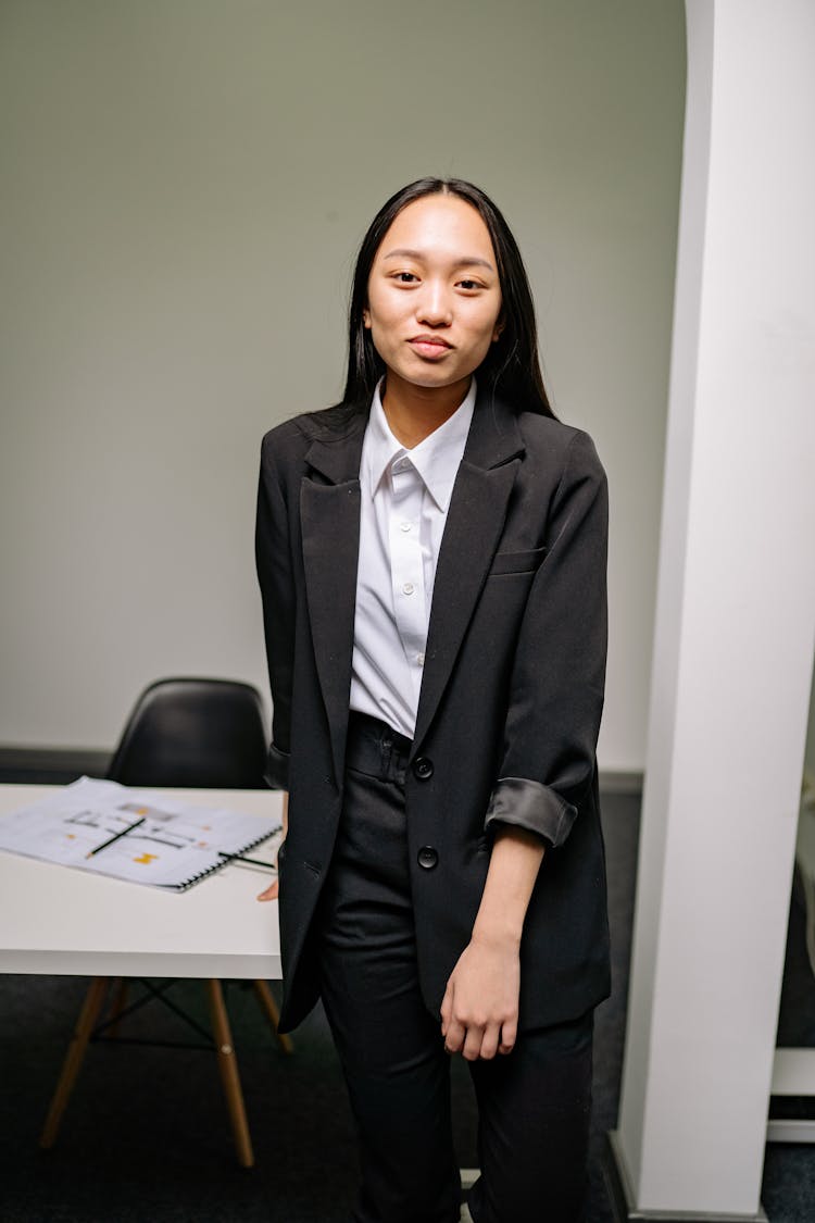 A Woman In Black Suit Standing Beside A Desk