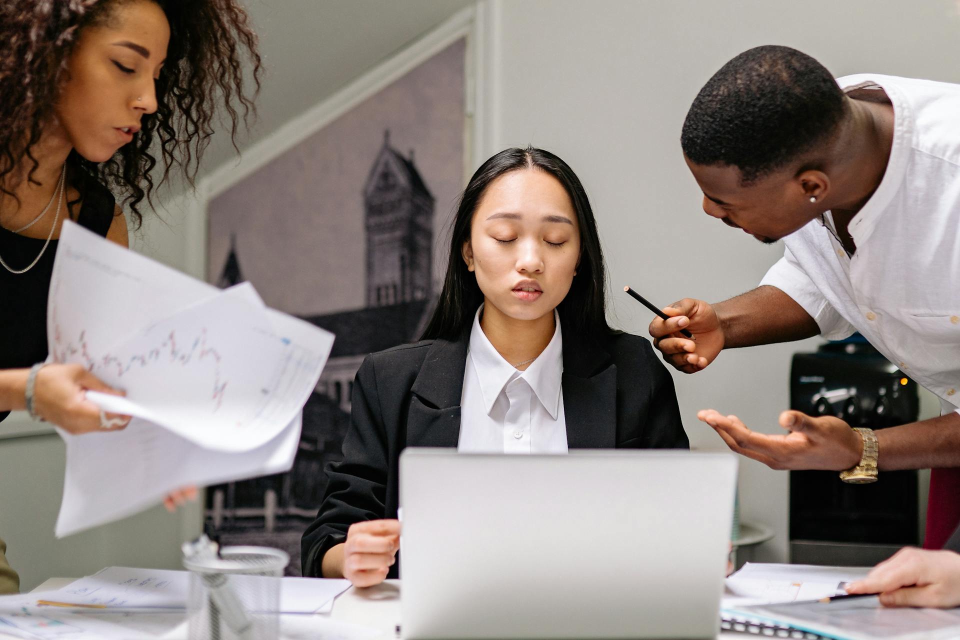 Three diverse coworkers engaged in a business discussion at an office desk.