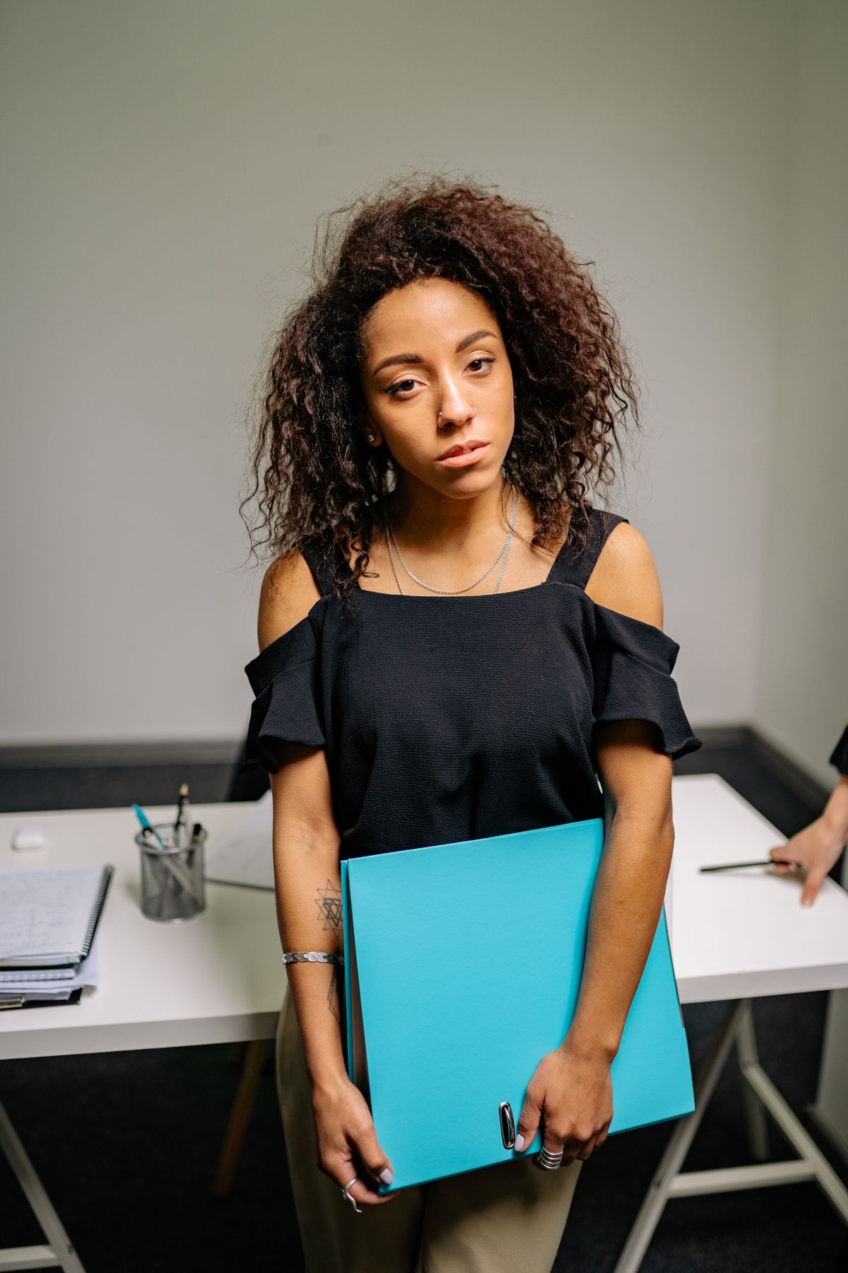 A Black woman in a striped blazer holding a blue folder in a modern office — Yolanda, for BossBabe Gangster (bossbabegangster.com)