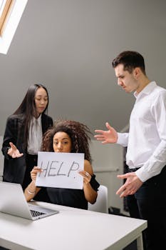 Woman holding HELP sign surrounded by colleagues in a tense office situation.
