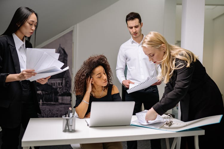 A Woman Sitting At The Table While Talking To Her Coworkers