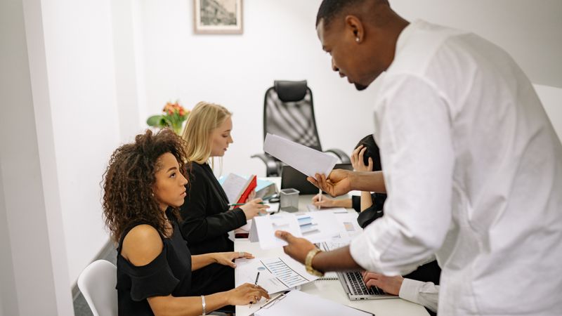 An office meeting where a man argues with a woman over documents, causing tension.