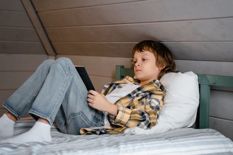 Photo by MART PRODUCTION on Pexels Un niño está acostado en una cama leyendo un libro en un acogedor dormitorio con decoración de madera. - Foto de MART PRODUCTION en Pexels