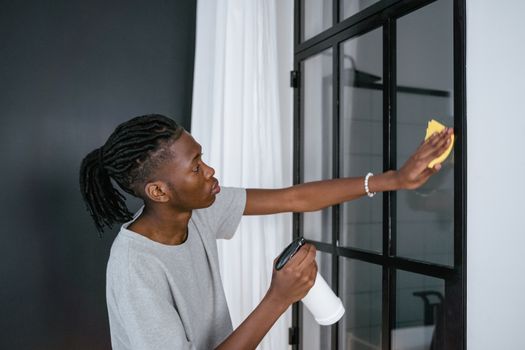 Young man cleaning window indoors using a spray bottle and cloth.