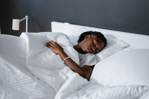 Free A man sleeping peacefully under a white blanket in a cozy bedroom. Stock Photo