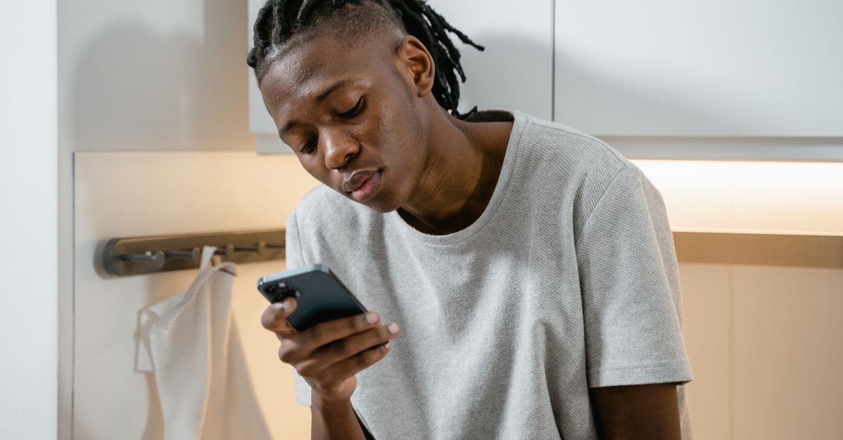 Indivíduo concentrado enviando mensagens pelo smartphone em um ambiente de cozinha moderna.