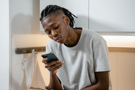 Focused individual texting on smartphone in modern kitchen environment.