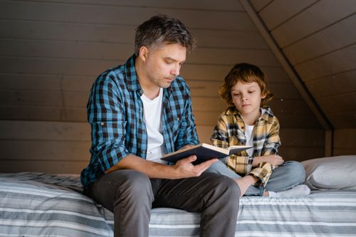 Free A man reads a book to his son in their cozy attic bedroom, bonding together. Stock Photo