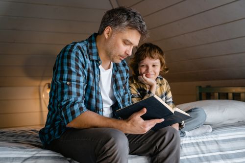 Free A father and son share a warm moment reading a book in a cozy attic bedroom. Stock Photo