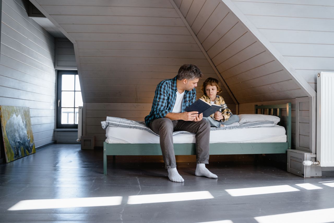 Father and son reading together in a cosy attic bedroom.