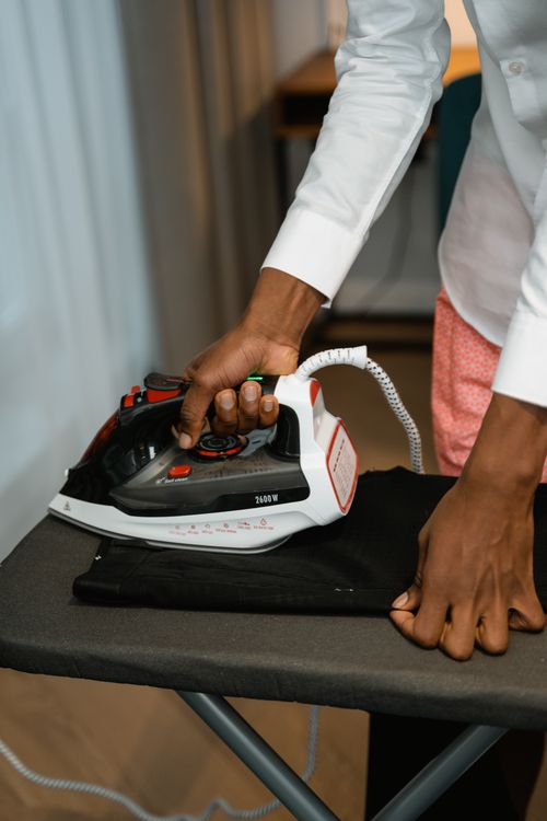 Free A person ironing black pants on an ironing board inside a home setting. Stock Photo