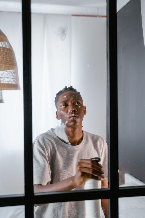 Free A young man spraying a cleaning product on a glass surface indoors. Stock Photo