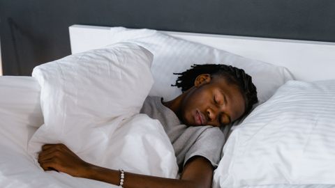 An adult sleeping peacefully on a bed with white pillows and linen.