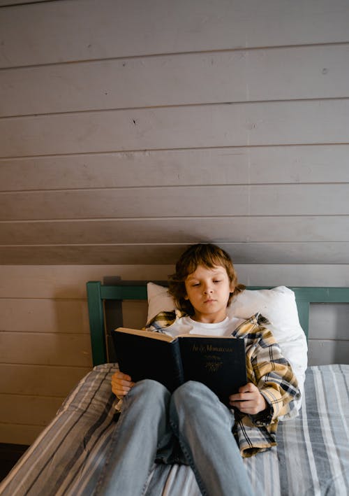 Free A Kid Reading a Book While Lying on the Bed Stock Photo