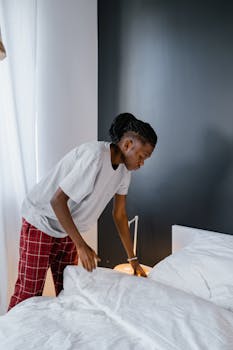 A young man tidying up a bed in a stylish, modern bedroom. Household chores indoors.