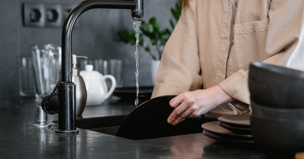 Iemand maakt het afvoerputje van een keukenspoelbak schoon met een borstel