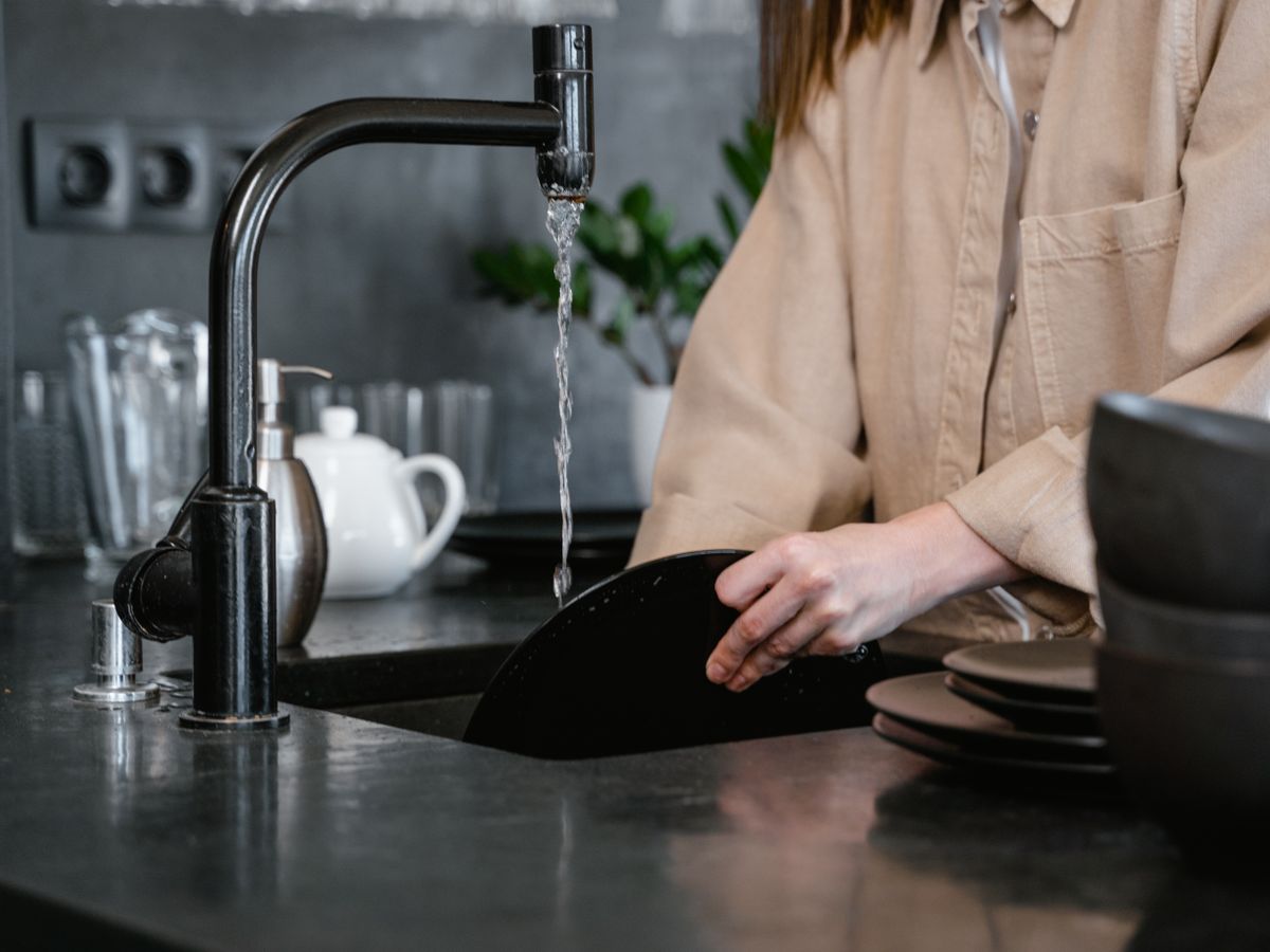 Close-up of a person washing dishes in a kitchen sink.