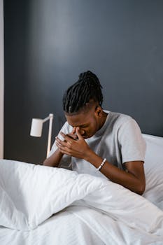 A man enjoys a warm cup of coffee while sitting in a cozy bed with white linens.