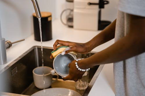 Free Close-up of woman washing dishes at kitchen sink, highlighting hands with bracelet. Stock Photo